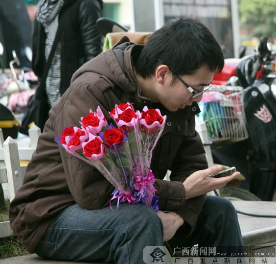 2月14日情人节当天,一位手捧九支玫瑰花的男生坐在路边