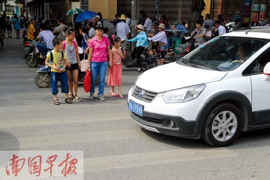 一辆白色小车,对车右侧想过马路的小学生视而不见.