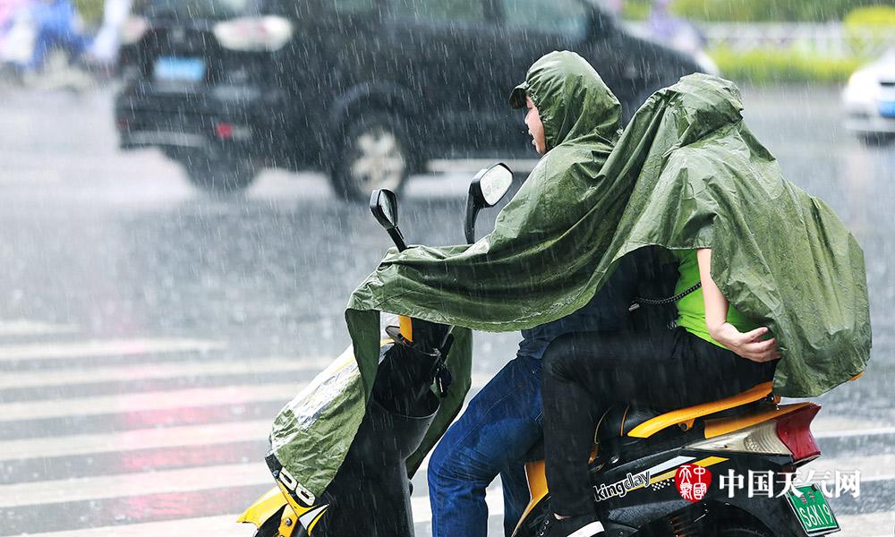 大雨如注,骑车出行的市民衣裤依然被雨水浸湿(摄影:刘英轶)