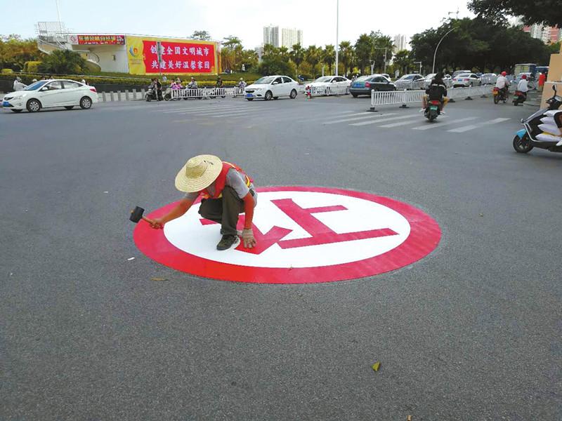 北京路和站前路交汇路口,施工人员在马路上贴上"让"字提醒车辆礼让行