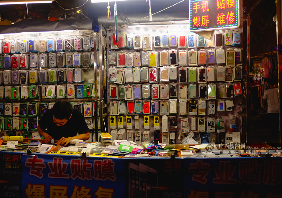 图为夜市里,一名卖手机壳的老板正在为顾客的手机贴膜.